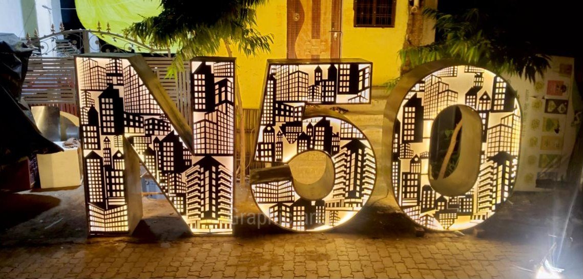The N50 metal cast installation by Graphic Arts for the Noida 50 years celebration — cut-metal numerals with a city skyline worked into their faces, lit from within at night