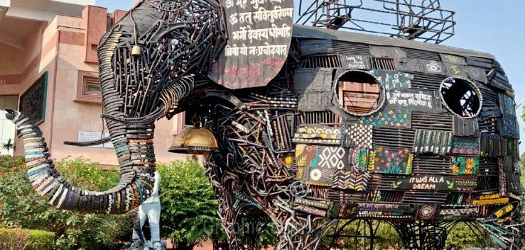 A monumental elephant assembled from reclaimed chain, pipe, gears and machine components, with painted decorative panels set into the body